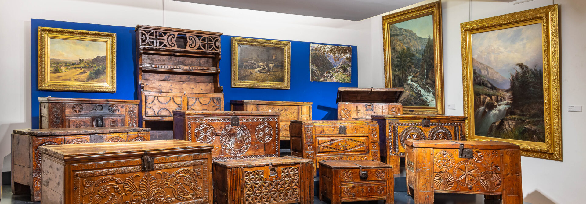 Des coffres en bois du Queyras sont présentés sur une estrade.