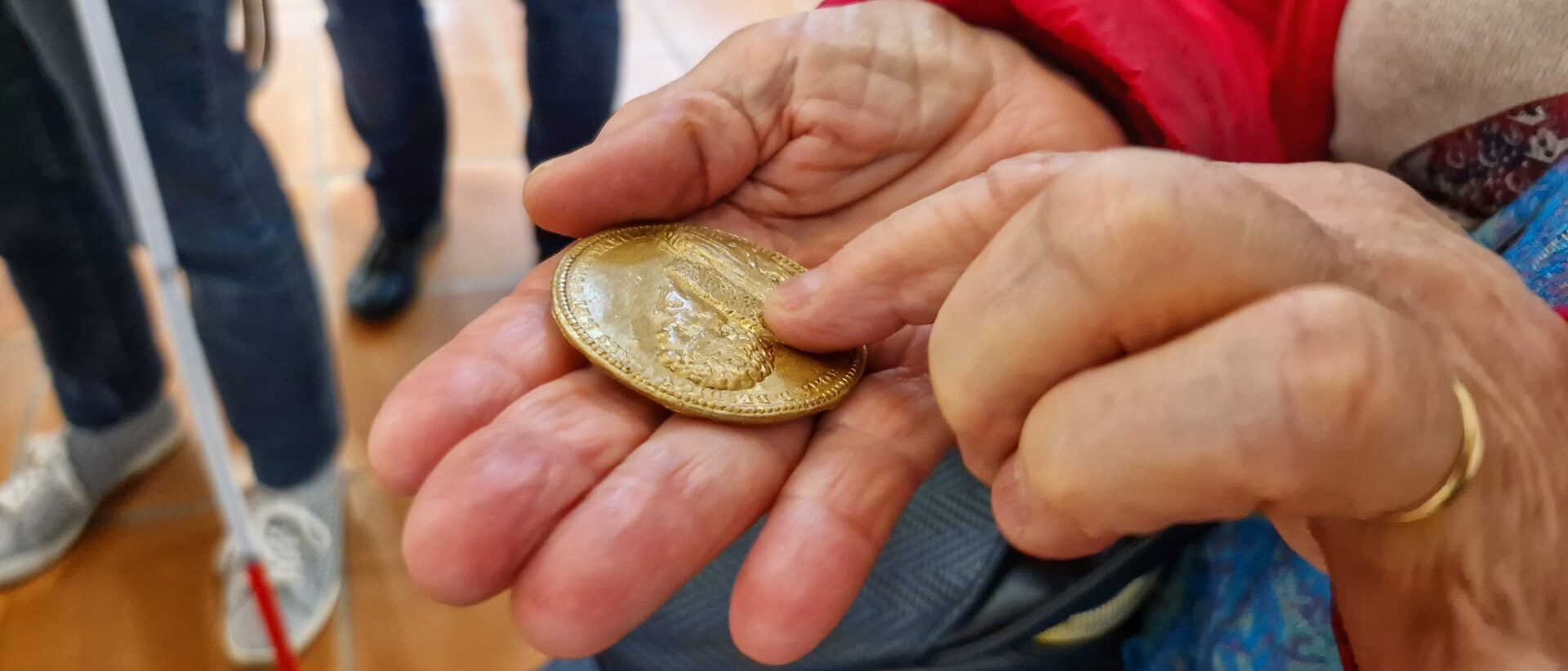 Une personne malvoyante touche une reproduction d'une pièce de monnaie à l'effigie du duc de Lesdiguières. - Agrandir l'image, fenêtre modale