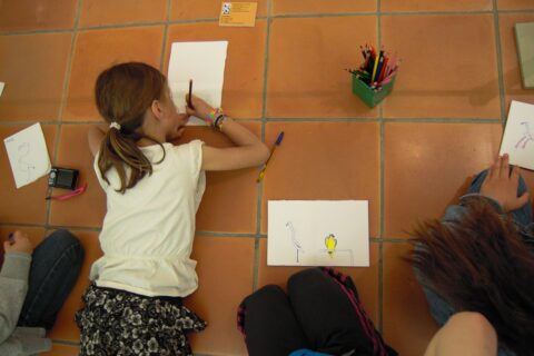Deux enfants dessinent sur des feuilles installées sur le sol du musée.
