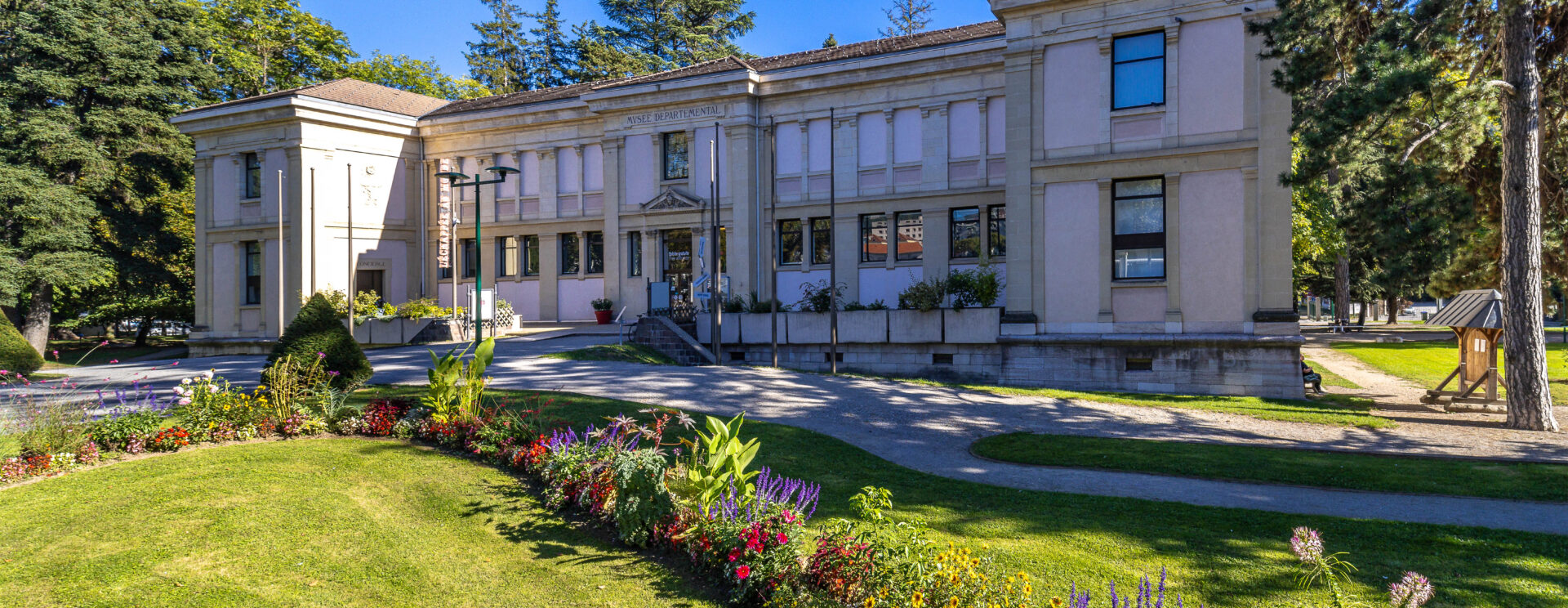 Vue du bâtiment du musée sous un beau ciel bleu avec un massif de fleurs présenté sur le devant de l'image.
