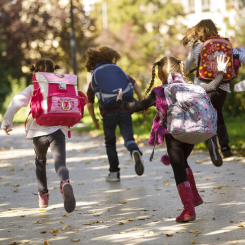 Six enfants de dos portant des cartables courent.